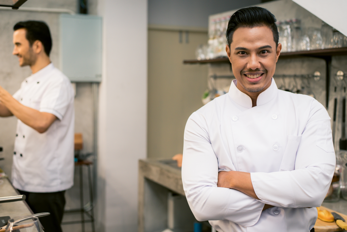 Smiling young asian chef in the kitchen interior of the restaura